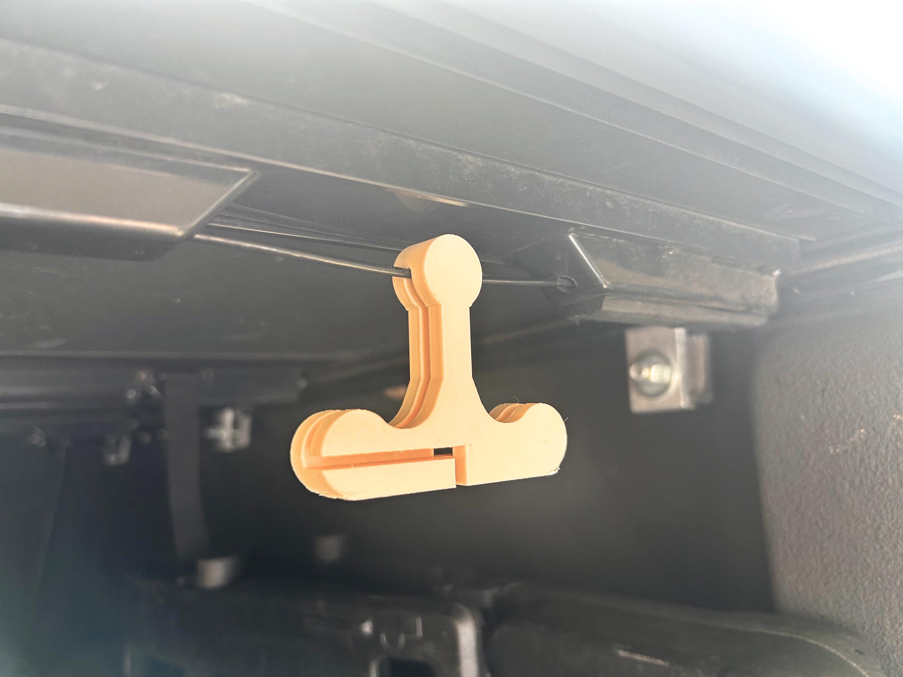 A beige handle hanging on the pull cord of a pickup truck bed cover. Designed to found located and pulled easier.