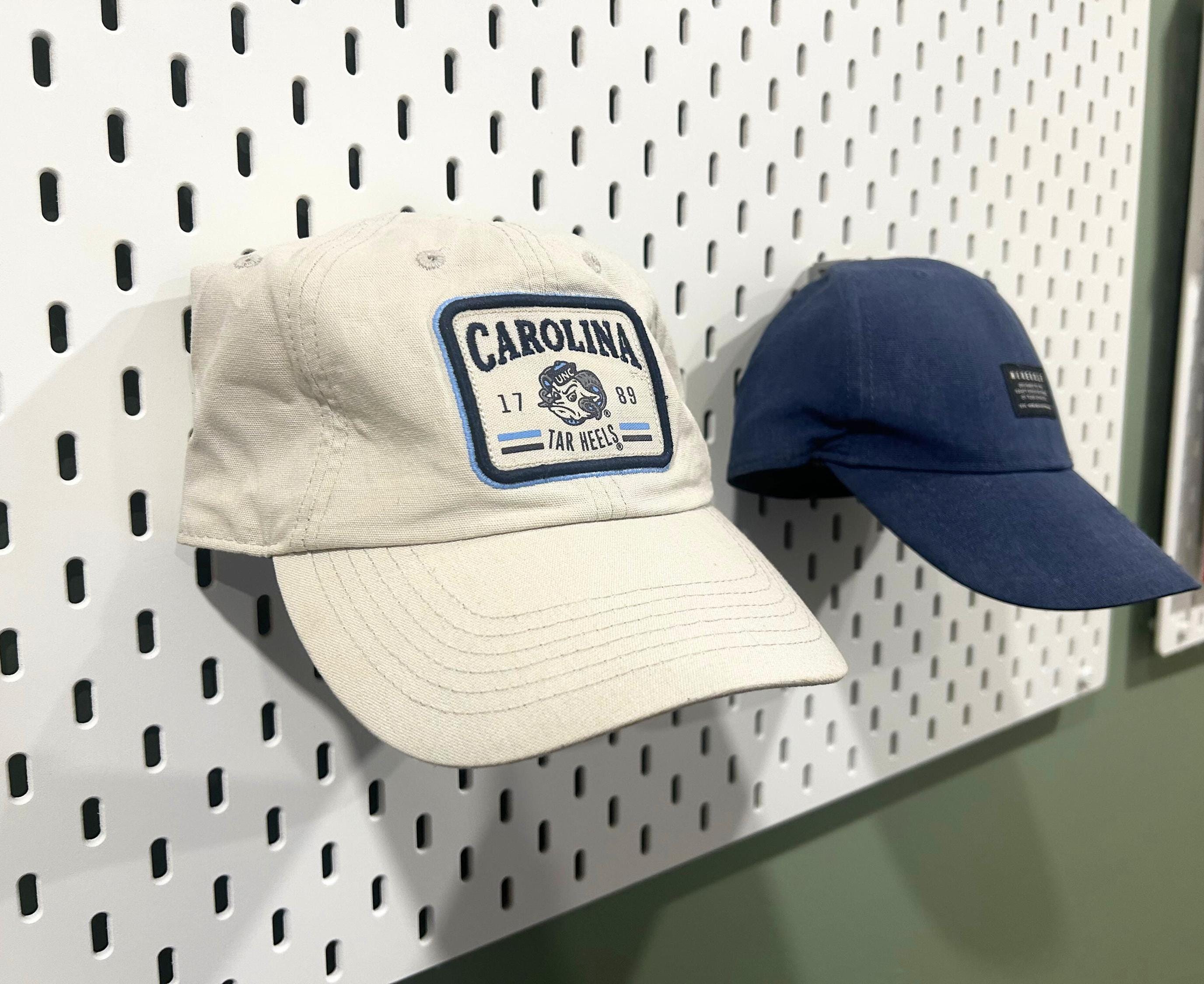 Two baseball caps hanging on a white Ikea Skadis pegboard. Both hung up with the Ikea Skadis hat display mounts.