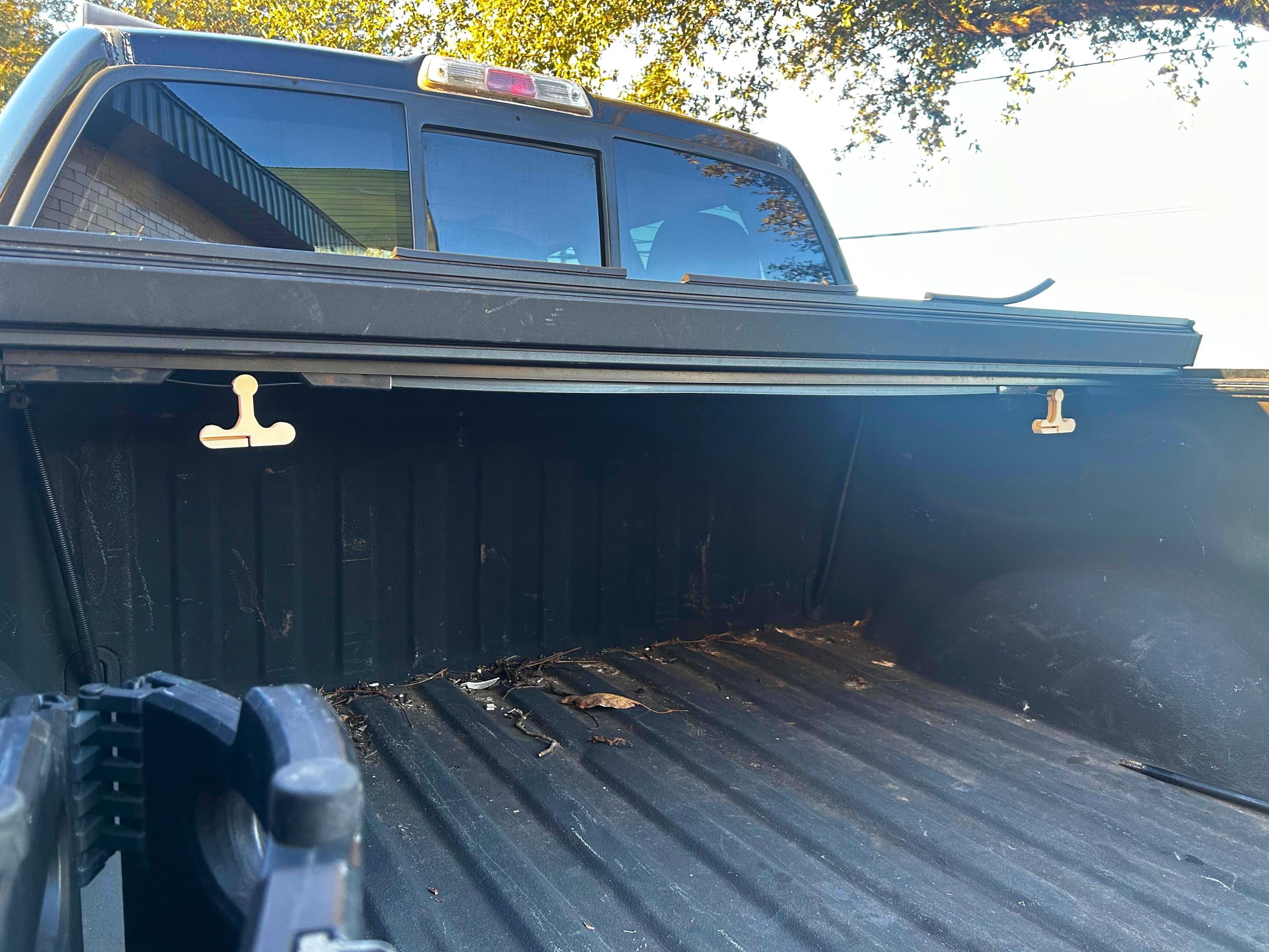 The inside of a black truck bed with two beige hooks attached to the bed cover.