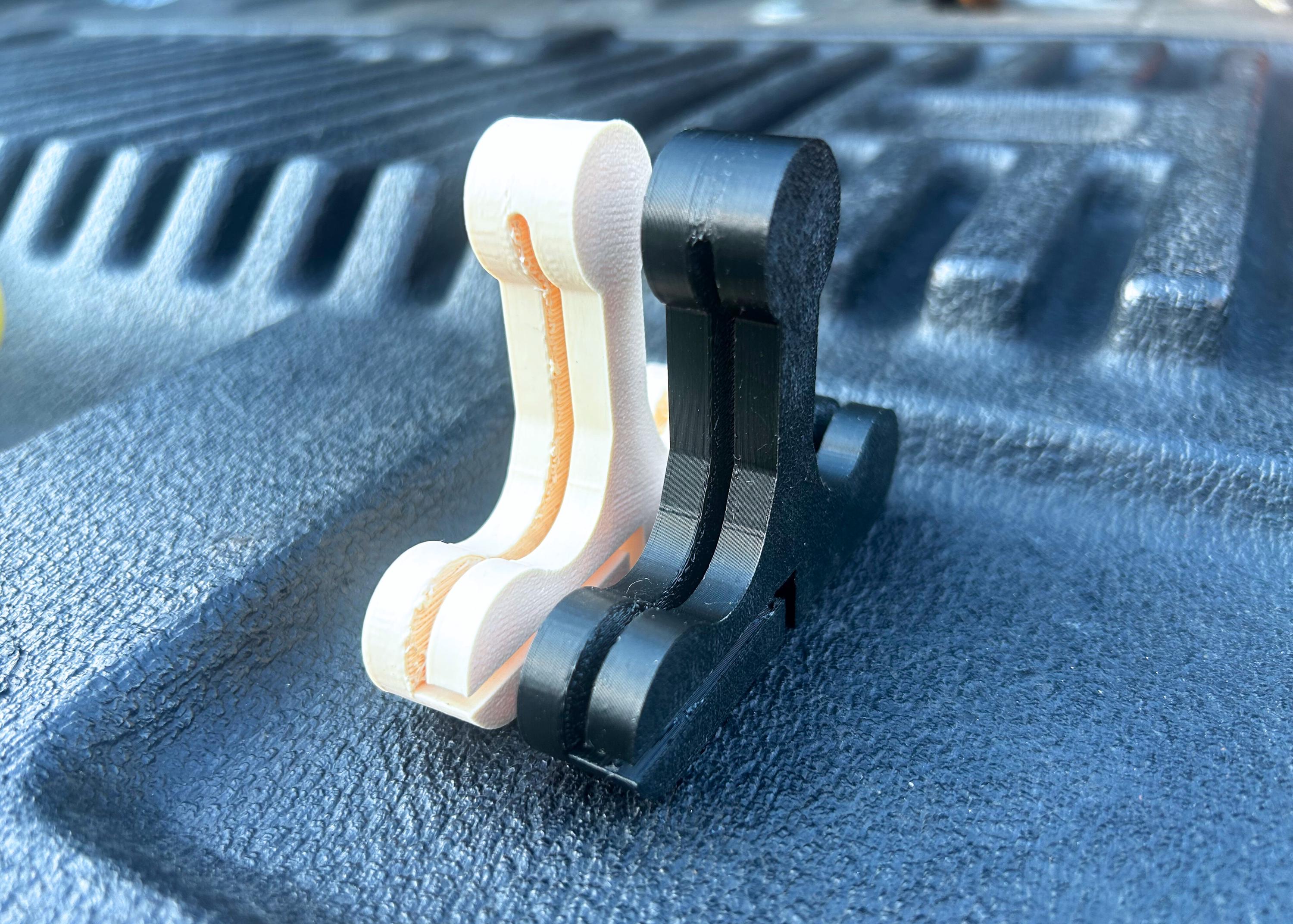 Two bed cover handles, one black, and one beige, sitting on a truck tailgate.