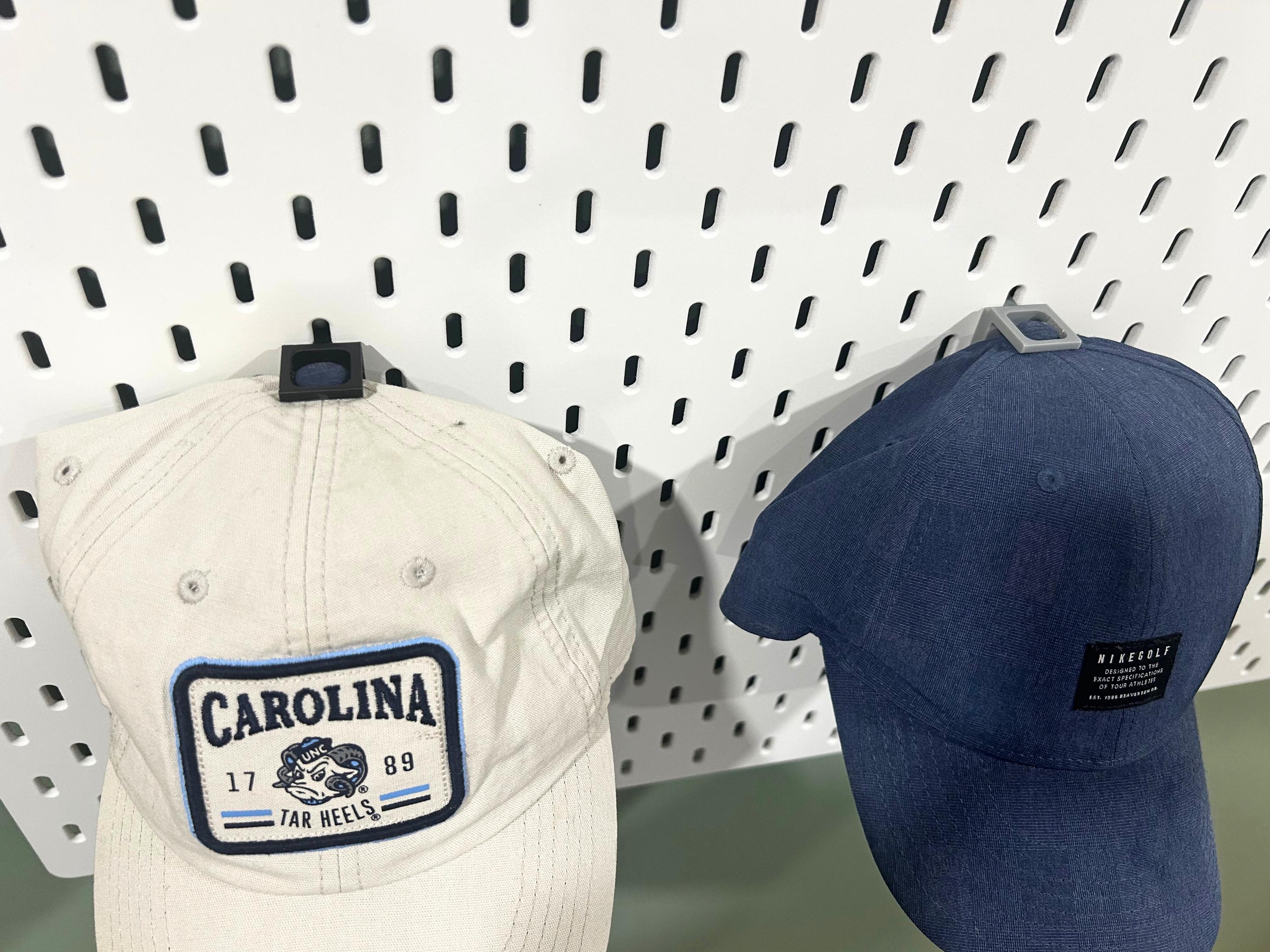 Shows the top view of two baseball caps hanging on a pegboard using Ikea Skadis hat display mounts.